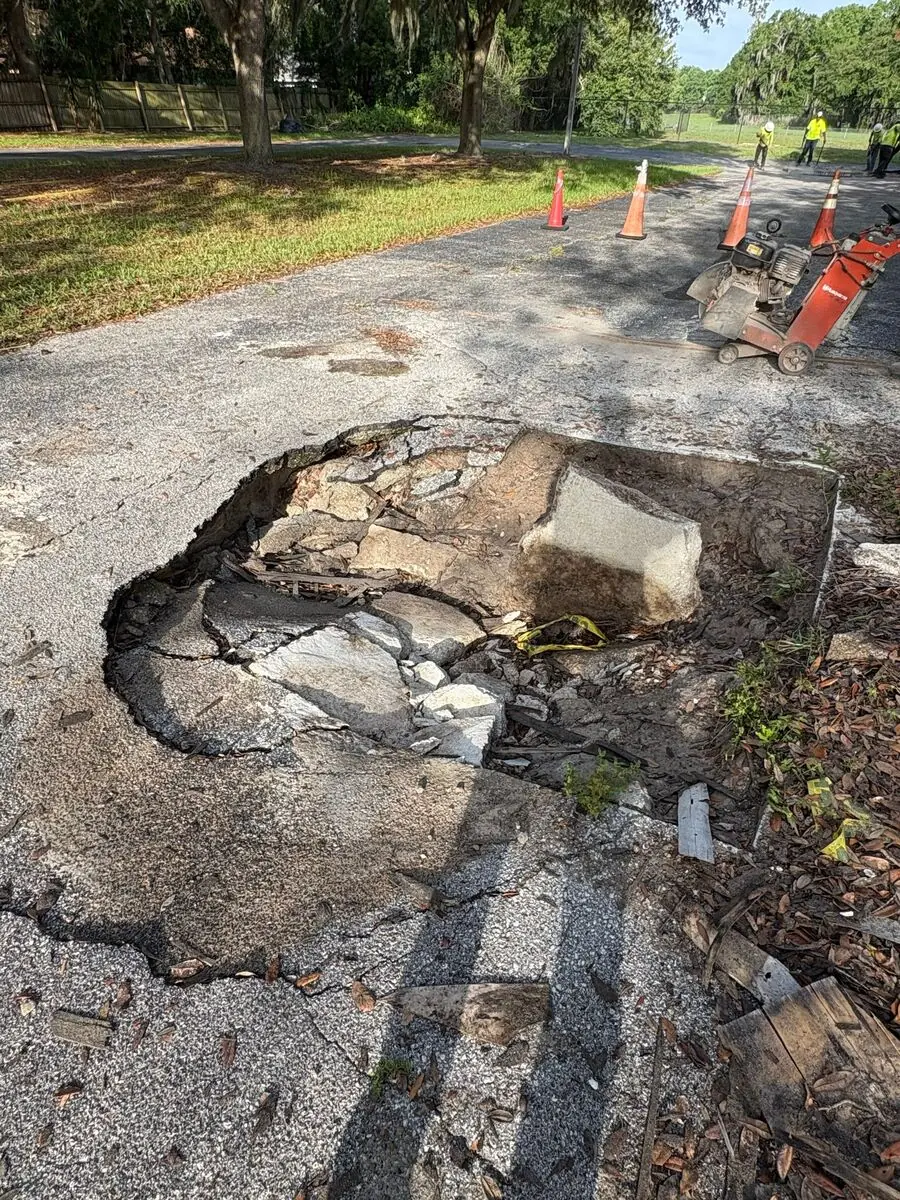 Advanced sinkhole with debris and exposed drainage grate in a Central Florida commercial lot